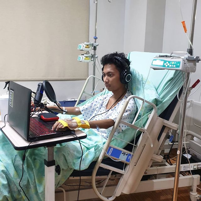 Emman Nimedez in a white hospital gown vlogging in his laptop.